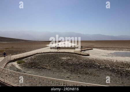 Tourists walking along the boardwalk and onto the sand flats at Badwater Basin in Death Valley National Park, California, USA, on a hazy summer day Stock Photo