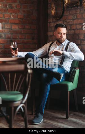Handsome young man enjoying a glass of red wine looking at his watch Stock Photo