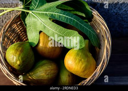 A few yellow figs in wicker basket on concrete background in sunshine. Stock Photo