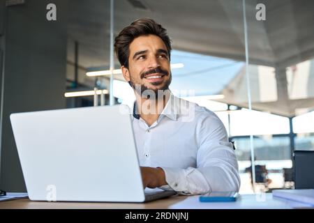 Smiling young Latin business man working at laptop computer in office. Stock Photo