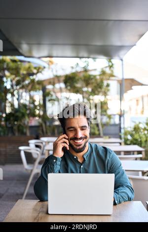 Happy Latin business man talking on mobile phone working on laptop outdoors. Stock Photo
