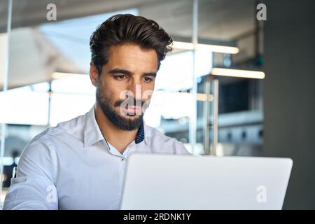 Busy young Latin business man looking at laptop using computer at work. Stock Photo