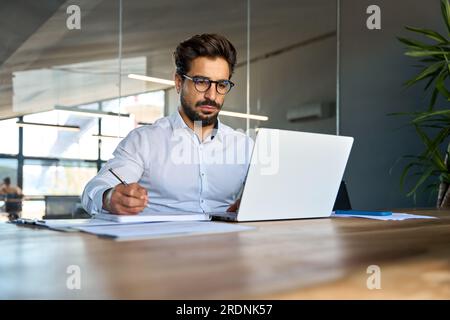 Busy professional young Latin business man working in office elearning looking at laptop. Stock Photo
