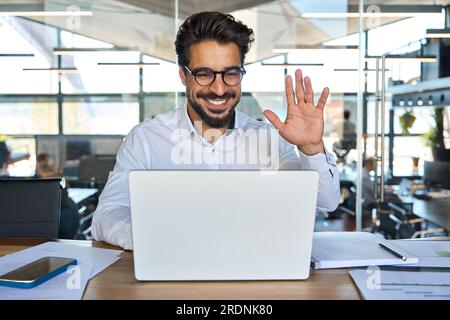 Happy young Latin business man working in office having hybrid meeting. Stock Photo