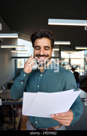 Smiling young Latin business man holding papers making call, vertical. Stock Photo