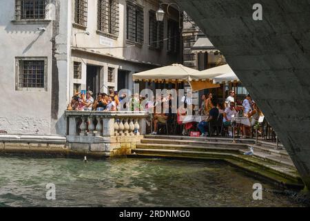 Waterfront cafè-restaurant on the Grand Canal, right next to Rialto Bridge, crowded with tourists in summer, Venice, Veneto, Italy Stock Photo