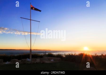Waving national australian flag facing rising sun over Pacific ocean at ...