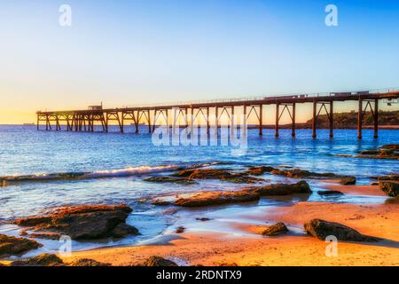 Long historic jetty at Middle Camp beach of Catherine hill bay coastal town in Australia from low tide sandy beach. Stock Photo