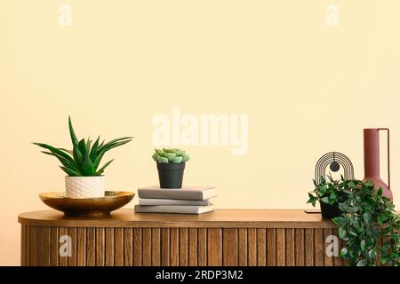 Green houseplants with books on chest of drawers near beige wall Stock Photo