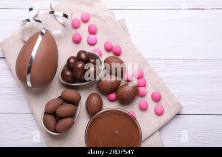 Delicious chocolate eggs, paste and candies on white wooden table, flat lay Stock Photo
