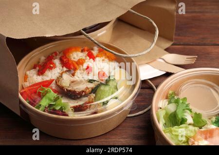 Tasty food in containers with knife and fork on wooden table Stock Photo