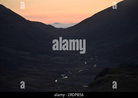 Early morning, dawn light on Wrynose Pass, Lake District National Park, Cumbria, UK, shows the valley and river in semi darkness; a pretty glow afar,  low mist, temperature inversion Stock Photo