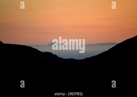 Early morning, dawn light on Wrynose Pass, Lake District National Park, Cumbria, UK, shows the valle river semi darkness; orange glow afar;  low mist, temperature inversion Stock Photo