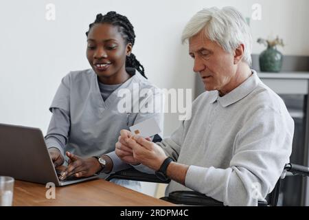 Portrait of white haired senior man holding credit card and learning to use online payment with nurse helping Stock Photo