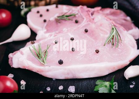 Raw pork meat. Fresh steaks with spices on slate board on black background. Side view. Stock Photo