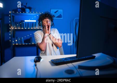 Shocked arabic gamer in headset at night near computer staring at ...