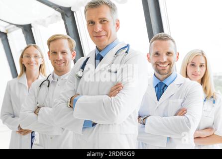 Successful team of medical doctors are looking at camera and smiling while standing with arms crossed in hospital Stock Photo