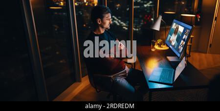 business man working late at night in an office, engaging in a video conference with his colleagues, contributing to his team's productivity and succe Stock Photo