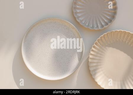 Three different size stoneware plates on beige table background. Flat lay, top view. Natural color disgware. Textured grainy pattern and scallop Stock Photo