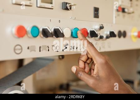 Closeup of black young man using control panel at factory focus on hand pushing button, copy space Stock Photo