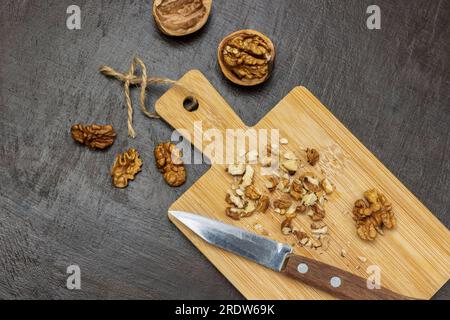 Crushed walnuts and knife on cutting board. Walnut shell and walnut kernels on the table. Flat lay. Brown background. Stock Photo