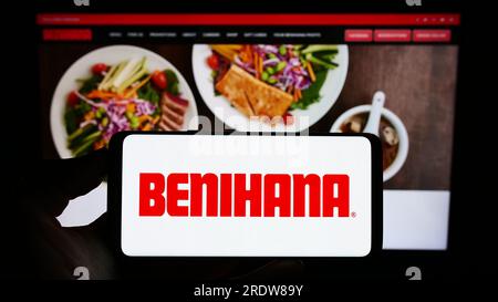 Person holding cellphone with logo of US restaurant company Benihana Inc. on screen in front of business webpage. Focus on phone display. Stock Photo