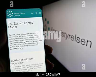 Person holding cellphone with web page of Danish energy agency Energistyrelsen on screen in front of logo. Focus on center of phone display. Stock Photo