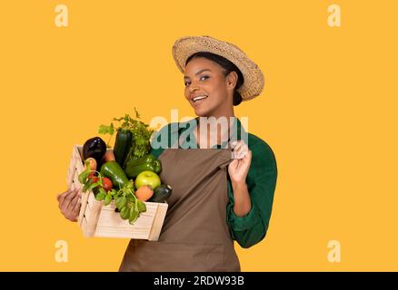 African Woman Posing With Vegetables In Box On Yellow Background Stock Photo