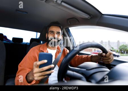 Happy arabic driver man holding smartphone using app in car Stock Photo