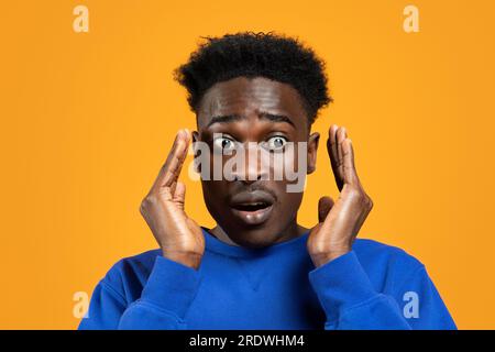 Shocked millennial african guy looking aside, yellow background Stock Photo