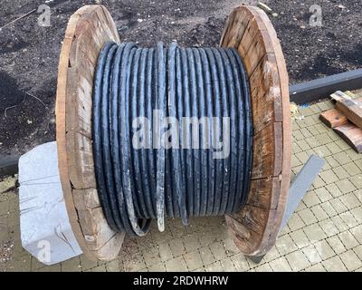 A thick electrical black cable rolled up on a large wooden roll lies on a green field on the Baltic island of Hiddensee. The cable should be laid unde Stock Photo