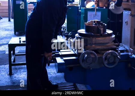 Large metal iron industrial turning and screw cutting machine for processing metal and parts with spare parts and a worker in a robe at the factory. Stock Photo