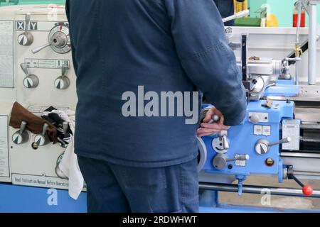 A male worker works on a larger metal iron locksmith lathe, equipment for repairs, metal work in a workshop at a metallurgical plant in a repair produ Stock Photo