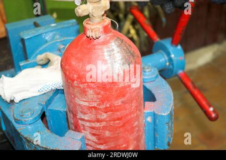 Blue iron metal large industrial vice and red fire extinguisher cylinder in the workshop at the plant. Stock Photo