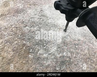 A sturdy, hard metal iron drill bit drills a hole in a large gray stone. Close view. The background. Stock Photo