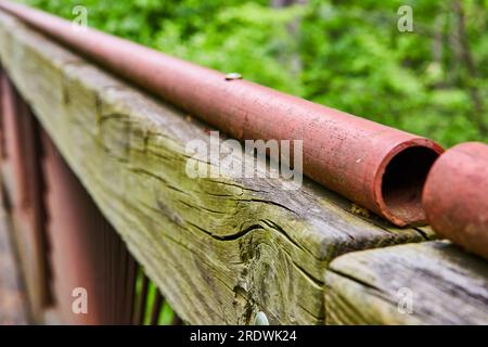 Long hollow red painted metal railing on top of weather worn green tinted wood beam at park Stock Photo