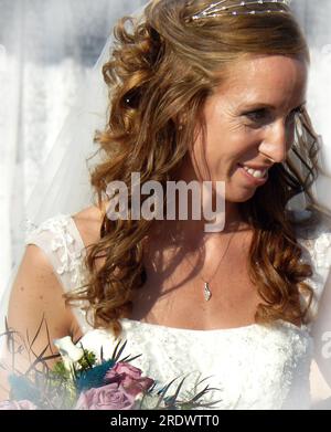 Bride smiles happily as she begins the outdoor wedding ceremony.  She is carrying a bouquet of roses.  Her dress is white and her veil. Stock Photo