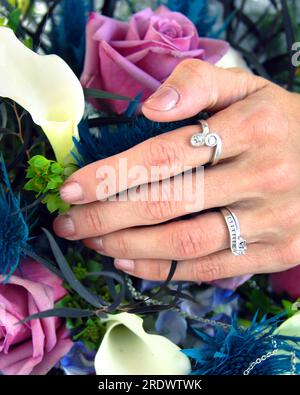 Bride lays her hand across her wedding bouquet.  Closeup shows her two white gold wedding rings. Stock Photo