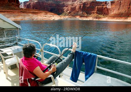 Woman fishes and enjoys view from a houseboat on Lake Powell. Stock Photo