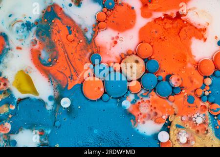 White milk with acrylic blue white yellow orange and gold paint poured on flat surface making a background asset Stock Photo