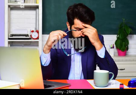 Online test. Tired student thinking about coursework. Overworked teacher working with laptop in school classroom. Educational process. Fatigued Stock Photo