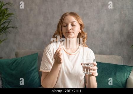 Beautiful young woman taking pills, sitting on couch at home. High quality photo Stock Photo