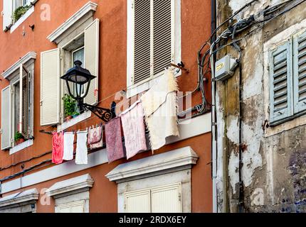 A picturesque street called 'Via della Pescheria' in the old city center of Trieste, with red walls and cloth lines, Trieste city center, Italy Stock Photo