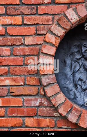 Vertical of red brick wall with half circle opening to black motif of wavy lions mane on right Stock Photo