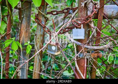 Wrapped rusting chains on rusty iron chain link fence with two corroding padlocks Stock Photo