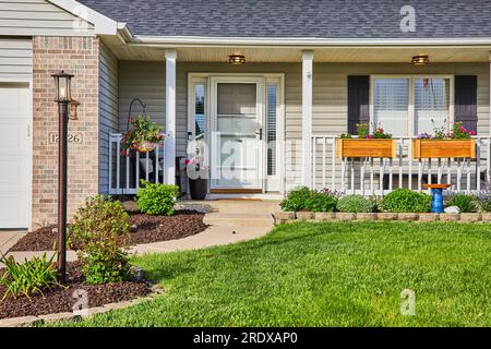 Landscaping tan, gray brick, gray siding house manicured lawn, light on lamp post pole flower box Stock Photo