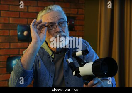 Senior man using telescope to look at stars in room Stock Photo