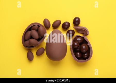 Delicious chocolate eggs and sweets on yellow background, flat lay Stock Photo