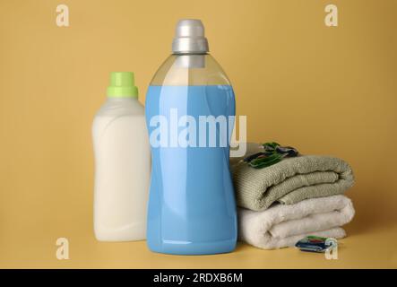 Bottles of fabric softener, laundry detergent capsules and stacked clean towels on pale yellow background Stock Photo