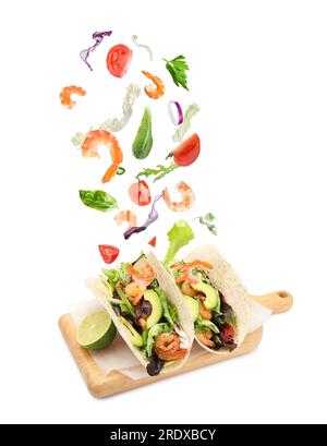 Delicious tacos. Ingredients falling into tortillas on white background Stock Photo